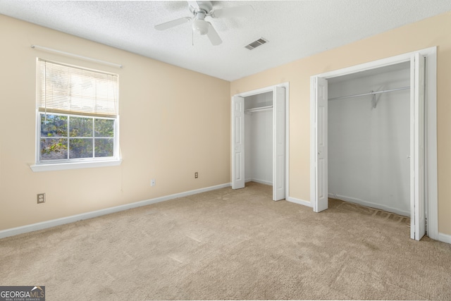 unfurnished bedroom featuring a textured ceiling, two closets, light colored carpet, and ceiling fan