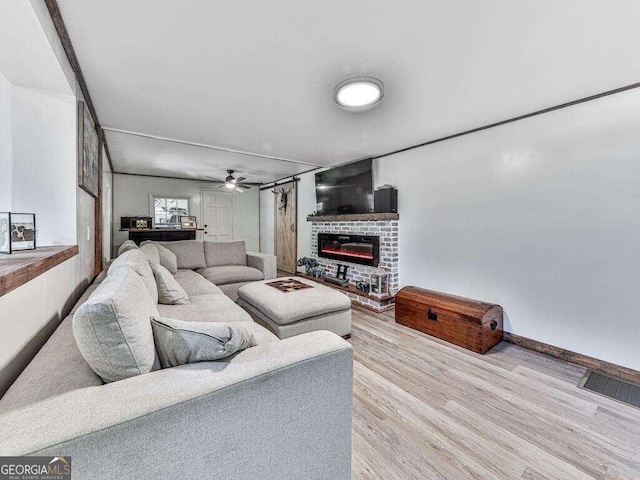 living room featuring a brick fireplace, light wood-type flooring, and ceiling fan