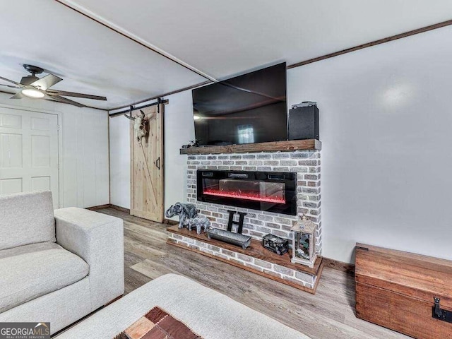 living room featuring ceiling fan, a barn door, light wood-type flooring, a brick fireplace, and ornamental molding