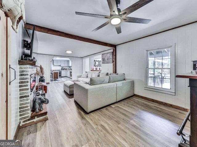 living room with wooden walls, a brick fireplace, light hardwood / wood-style floors, and ceiling fan