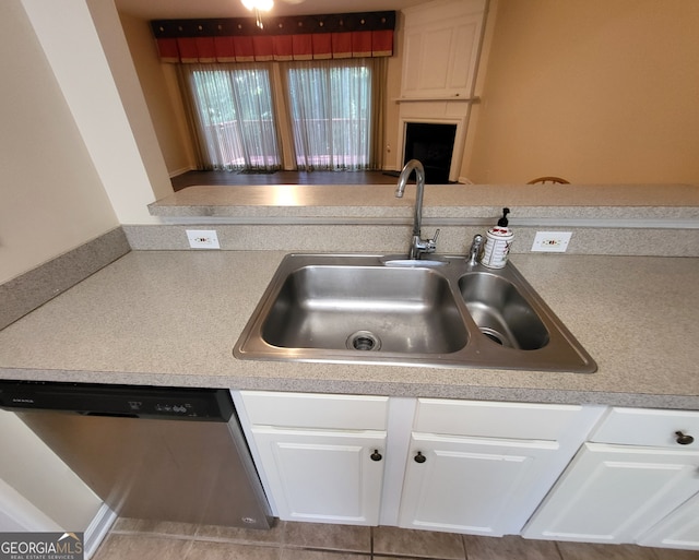 kitchen with tile patterned floors, a large fireplace, sink, stainless steel dishwasher, and white cabinetry