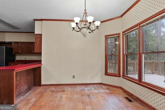 unfurnished dining area with a chandelier, light hardwood / wood-style floors, a wealth of natural light, and crown molding