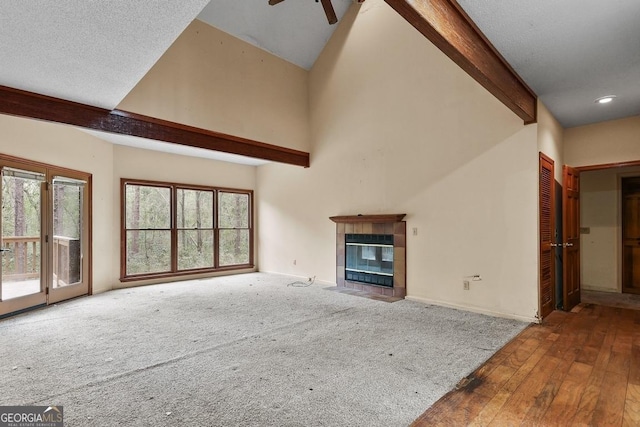 unfurnished living room featuring a tiled fireplace, ceiling fan, beamed ceiling, and a textured ceiling