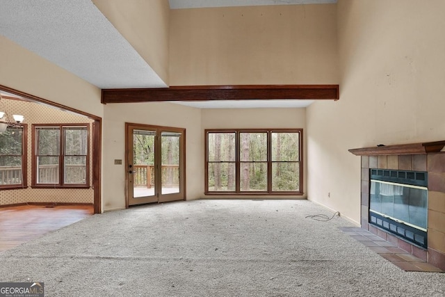 unfurnished living room featuring a tile fireplace, light carpet, a chandelier, and a wealth of natural light