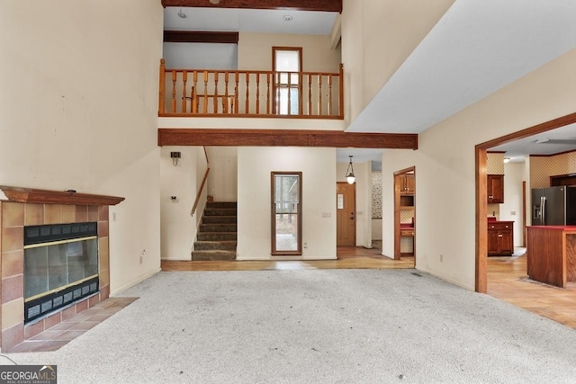 unfurnished living room with a tile fireplace, light carpet, and a towering ceiling