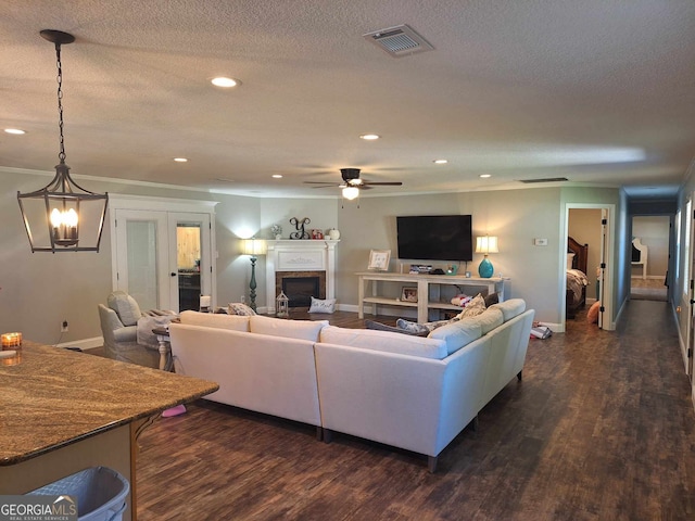 living room featuring dark wood-type flooring, ceiling fan with notable chandelier, and a textured ceiling