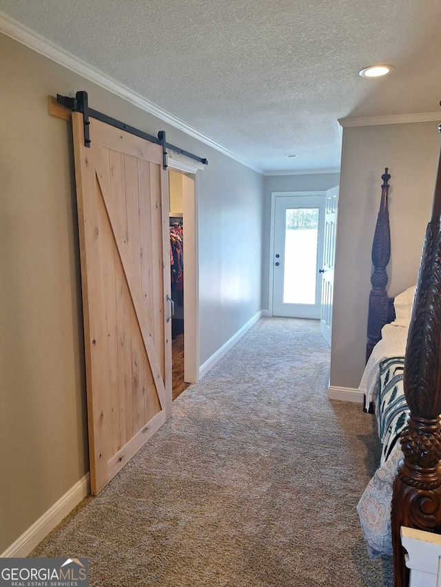 hallway featuring carpet floors, ornamental molding, a barn door, and a textured ceiling