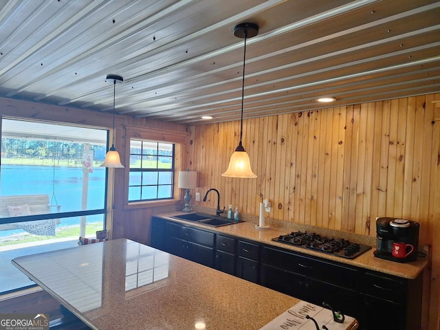 kitchen featuring sink, wooden walls, pendant lighting, black gas cooktop, and light stone countertops