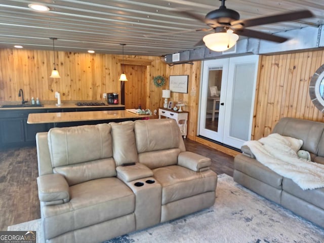 living room featuring hardwood / wood-style flooring, ceiling fan, sink, and wood walls