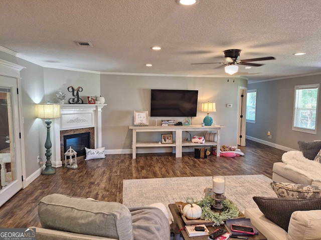 living room featuring a fireplace, ornamental molding, ceiling fan, dark wood-type flooring, and a textured ceiling