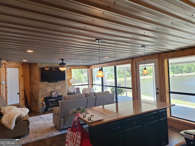 kitchen featuring dark wood-type flooring, hanging light fixtures, wooden ceiling, a wood stove, and a kitchen island