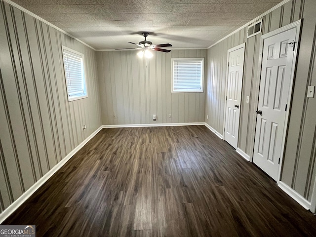 empty room with crown molding, dark hardwood / wood-style floors, ceiling fan, and a wealth of natural light