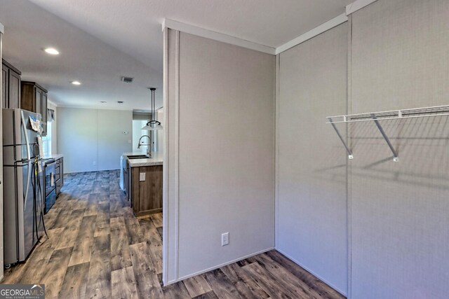 kitchen featuring wall chimney range hood, appliances with stainless steel finishes, sink, dark hardwood / wood-style floors, and a center island with sink