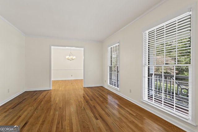 spare room with a chandelier, baseboards, wood finished floors, and crown molding