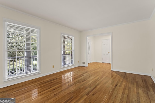 empty room with crown molding, wood finished floors, and baseboards