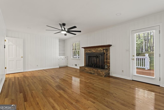 unfurnished living room with ceiling fan, baseboards, a fireplace, wood finished floors, and built in shelves