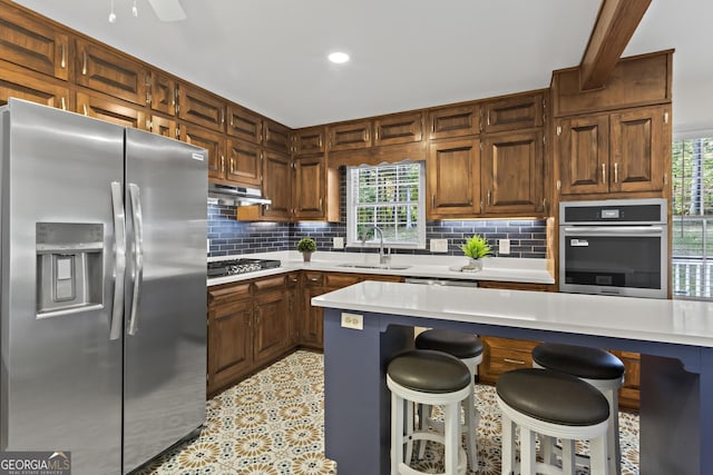 kitchen featuring a sink, under cabinet range hood, backsplash, light countertops, and appliances with stainless steel finishes