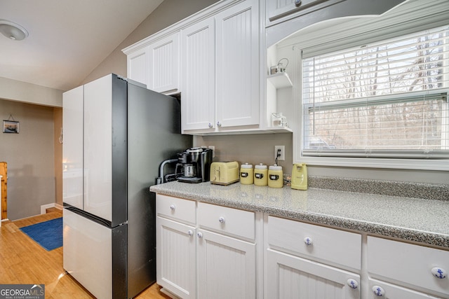 kitchen with lofted ceiling, white cabinets, light stone countertops, stainless steel refrigerator, and light hardwood / wood-style flooring