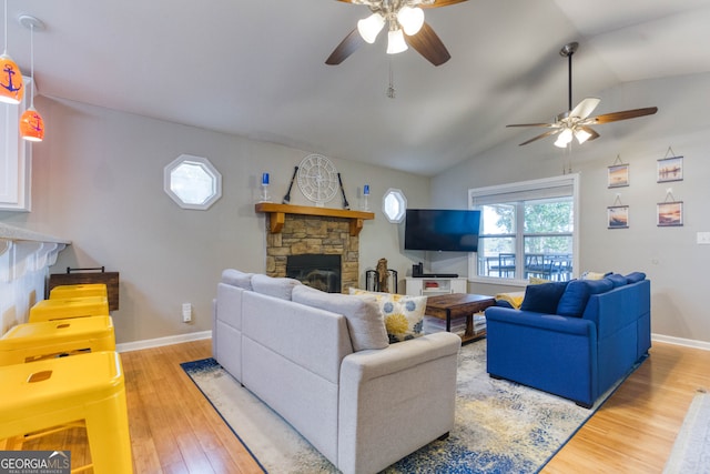 living room with ceiling fan, vaulted ceiling, light wood-type flooring, and a fireplace