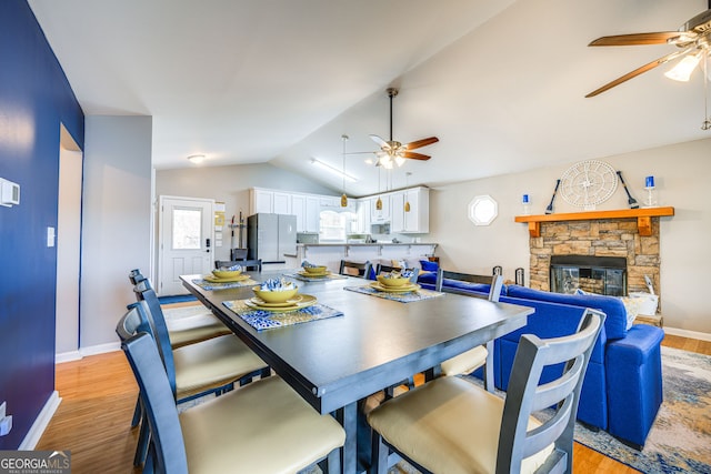 dining room featuring vaulted ceiling, a fireplace, light hardwood / wood-style floors, and ceiling fan