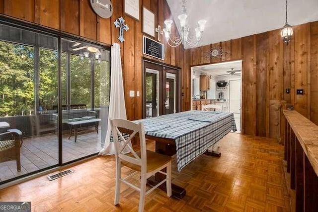 dining space with parquet flooring, a towering ceiling, ceiling fan with notable chandelier, and wood walls