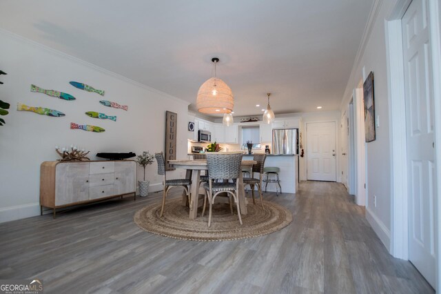 kitchen featuring hanging light fixtures, white cabinetry, wood-type flooring, crown molding, and stainless steel appliances