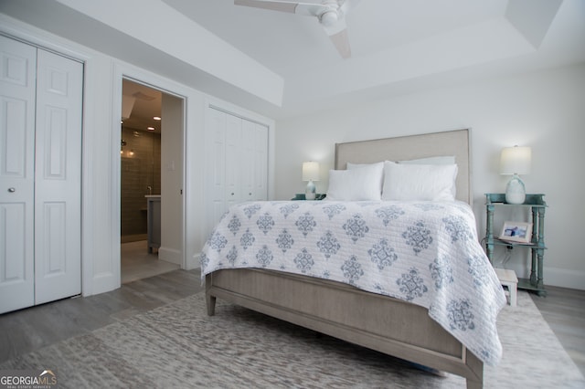 bedroom with dark wood-type flooring, ceiling fan, and multiple closets