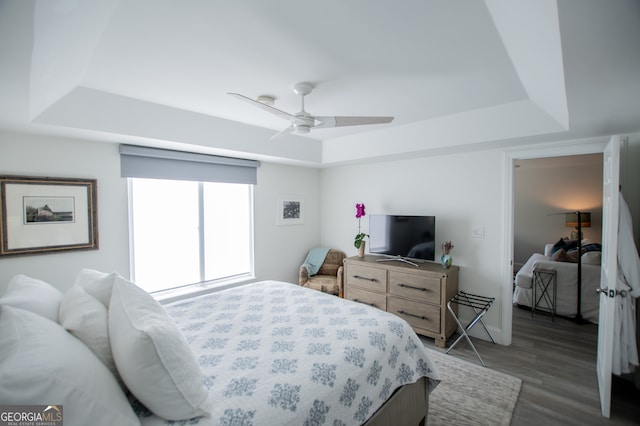 bedroom with ceiling fan, a raised ceiling, and dark hardwood / wood-style flooring