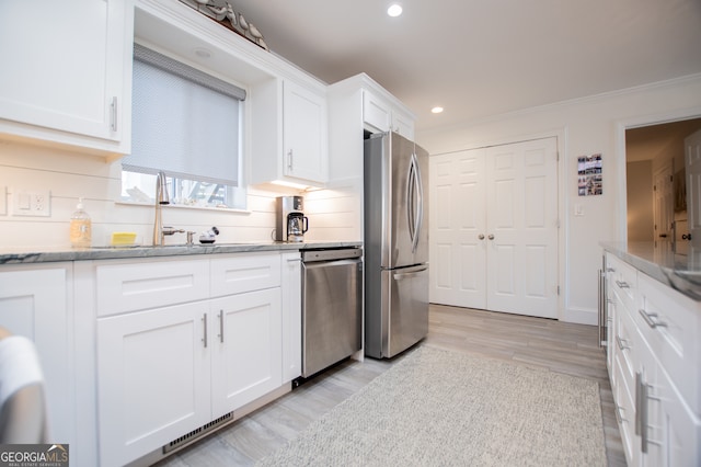 kitchen with tasteful backsplash, sink, stainless steel appliances, white cabinets, and light hardwood / wood-style flooring