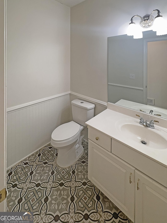 bathroom with toilet, vanity, wainscoting, and tile patterned floors