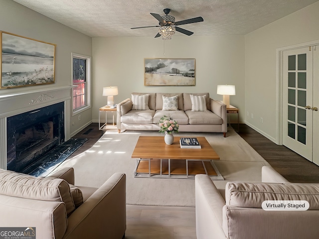 living area featuring a textured ceiling, ceiling fan, wood finished floors, a premium fireplace, and baseboards