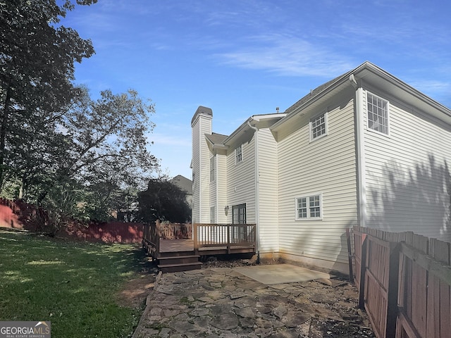 back of property with a wooden deck, a chimney, and a patio