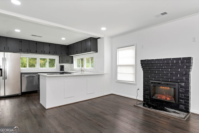 kitchen with appliances with stainless steel finishes, dark hardwood / wood-style flooring, kitchen peninsula, a brick fireplace, and ornamental molding