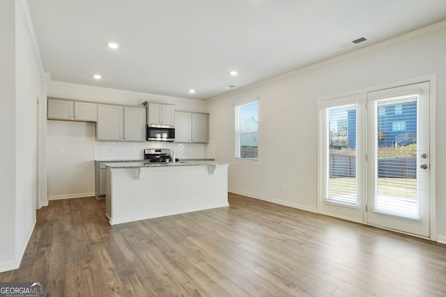 kitchen featuring a center island with sink, gray cabinetry, stainless steel appliances, and wood-type flooring