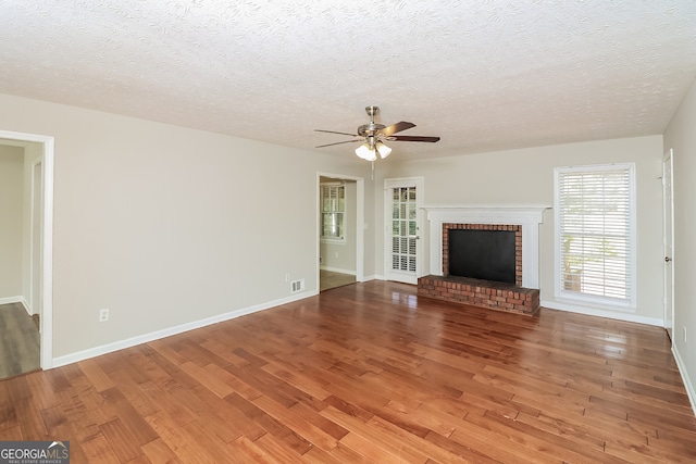 unfurnished living room with a brick fireplace, a textured ceiling, hardwood / wood-style flooring, and ceiling fan