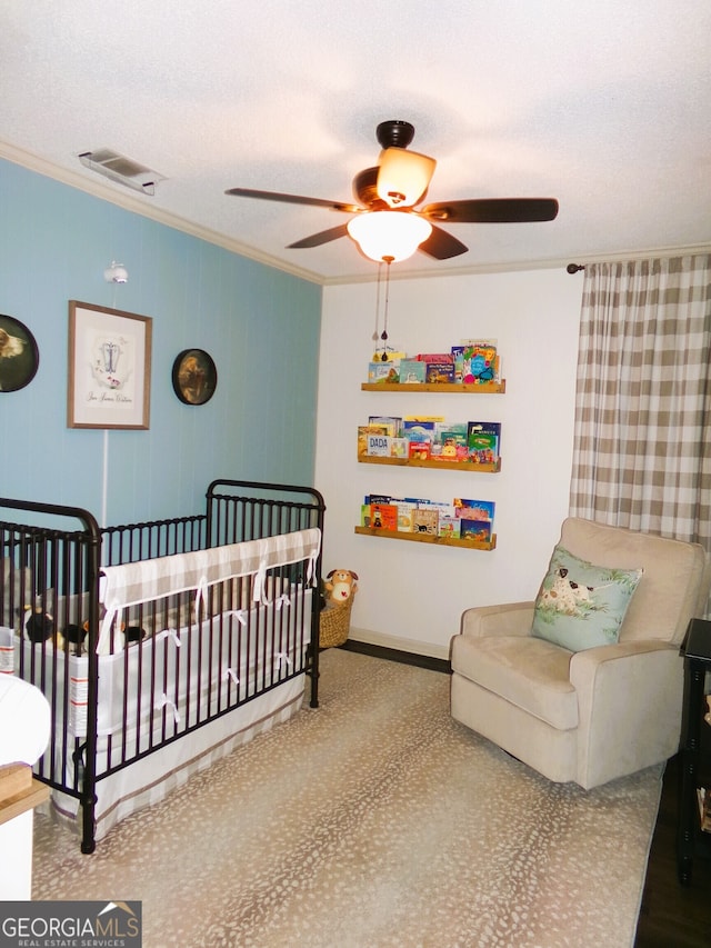 bedroom with crown molding, a textured ceiling, a crib, and ceiling fan