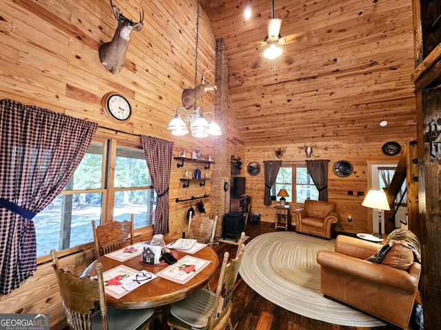 dining room with wood walls, ceiling fan with notable chandelier, high vaulted ceiling, and hardwood / wood-style floors