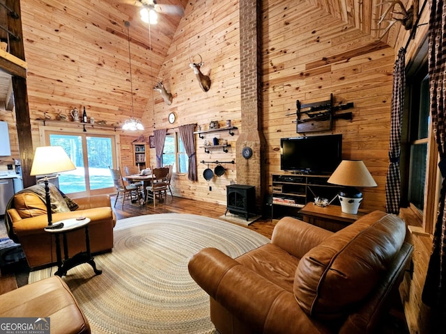 living room with hardwood / wood-style flooring, ceiling fan, high vaulted ceiling, a wood stove, and wooden walls