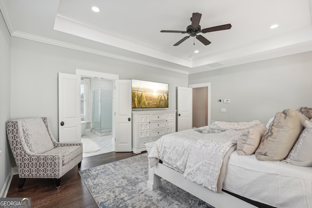 bedroom featuring dark wood-type flooring, ensuite bath, ornamental molding, a raised ceiling, and ceiling fan