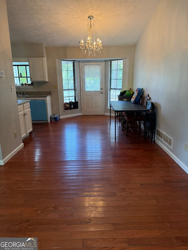 unfurnished dining area featuring a notable chandelier, dark hardwood / wood-style floors, and a textured ceiling