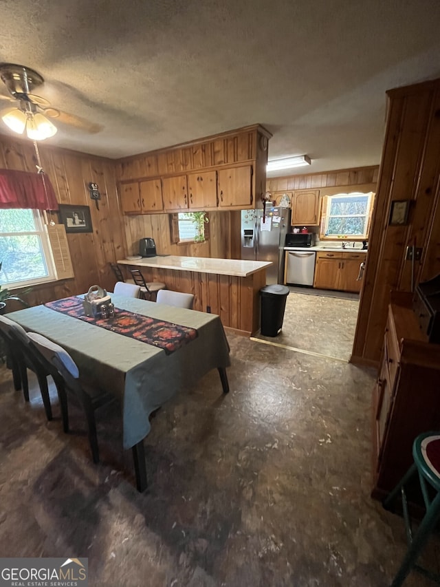 dining room with wood walls, a textured ceiling, and ceiling fan