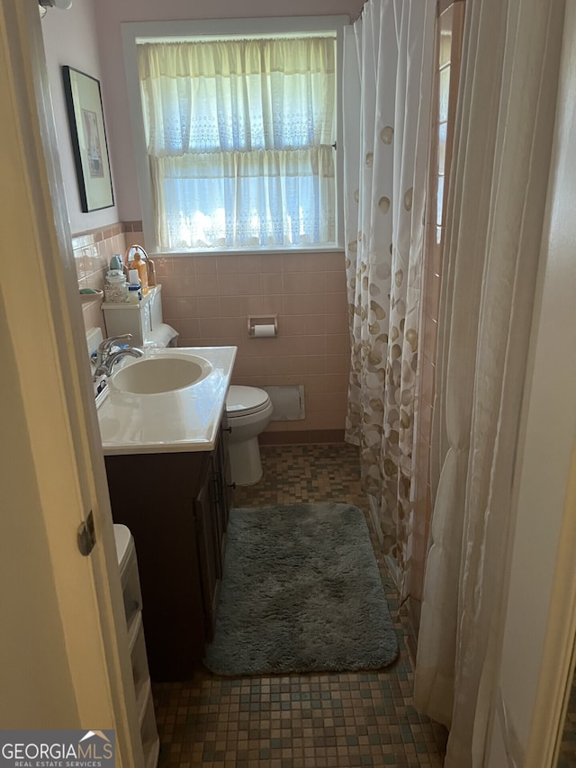 bathroom with toilet, a shower with shower curtain, vanity, and tile walls