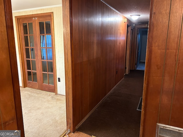 hallway with french doors, wood walls, a textured ceiling, and light colored carpet