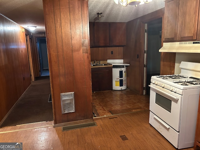 kitchen featuring wood walls, wood-type flooring, a textured ceiling, and gas range gas stove