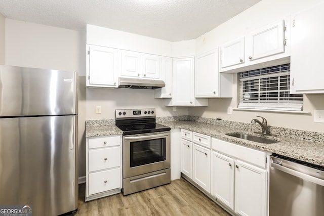 kitchen with light stone countertops, appliances with stainless steel finishes, sink, white cabinets, and light hardwood / wood-style flooring