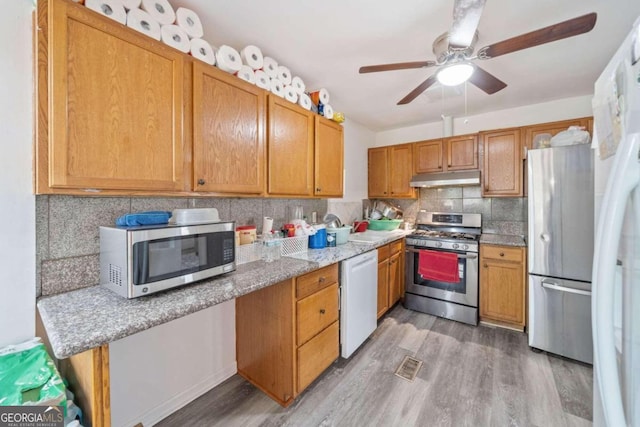 kitchen with appliances with stainless steel finishes, backsplash, ceiling fan, light stone counters, and light hardwood / wood-style flooring