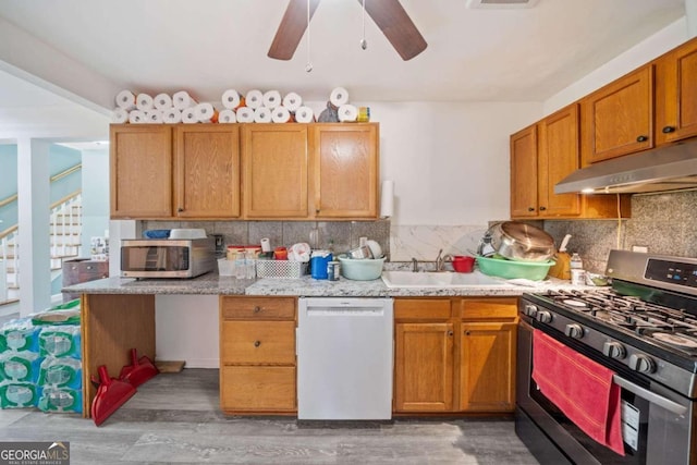 kitchen featuring tasteful backsplash, appliances with stainless steel finishes, hardwood / wood-style floors, ceiling fan, and light stone counters