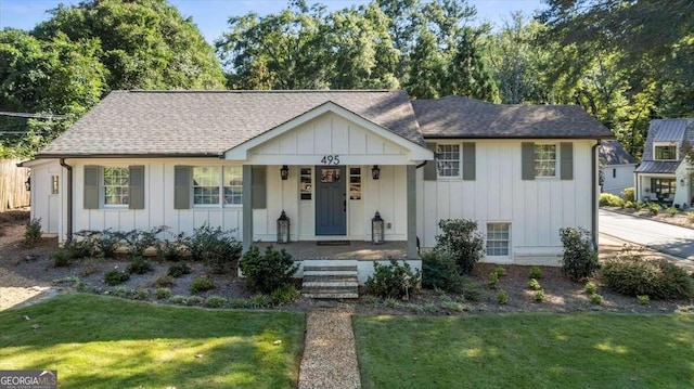 view of front facade featuring board and batten siding, a shingled roof, a front lawn, and covered porch