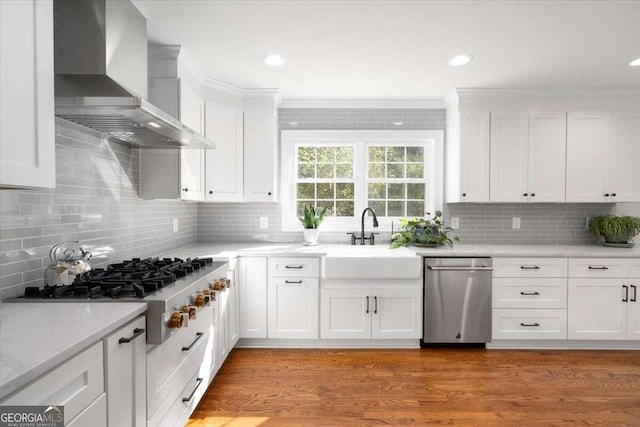 kitchen featuring wall chimney range hood, stainless steel appliances, light countertops, backsplash, and white cabinetry