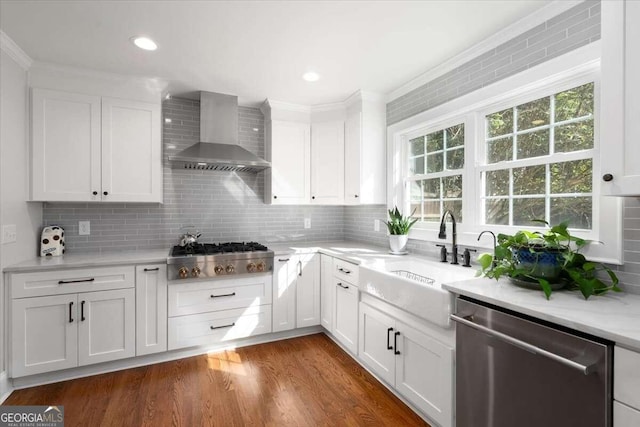 kitchen with stainless steel appliances, light countertops, wall chimney range hood, a sink, and white cabinetry